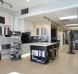 A professional kitchen remodeling showroom from TradeMark Construction LLC in Baltimore, MD, featuring a modern dark wood island, custom white cabinetry displays, and various countertop material samples.