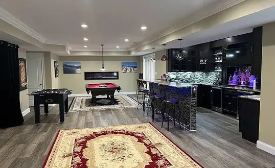 Finished basement and entertainment area featuring a modern wet bar with dark custom cabinetry, professional billiard table, and foosball station, showcasing luxury interior remodeling in Baltimore, MD.