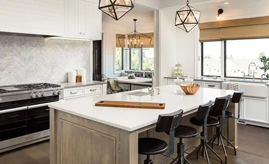 A luxury kitchen remodeling project in Baltimore, MD, featuring a large white island, industrial pendant lighting, and a grey herringbone tile backsplash.