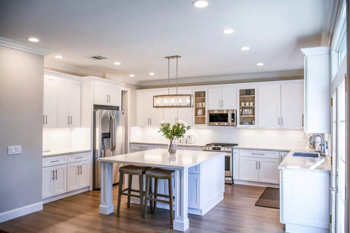 A modern kitchen remodel in Baltimore MD featuring bright white cabinets, stainless steel appliances, a large center island, and contemporary lighting.