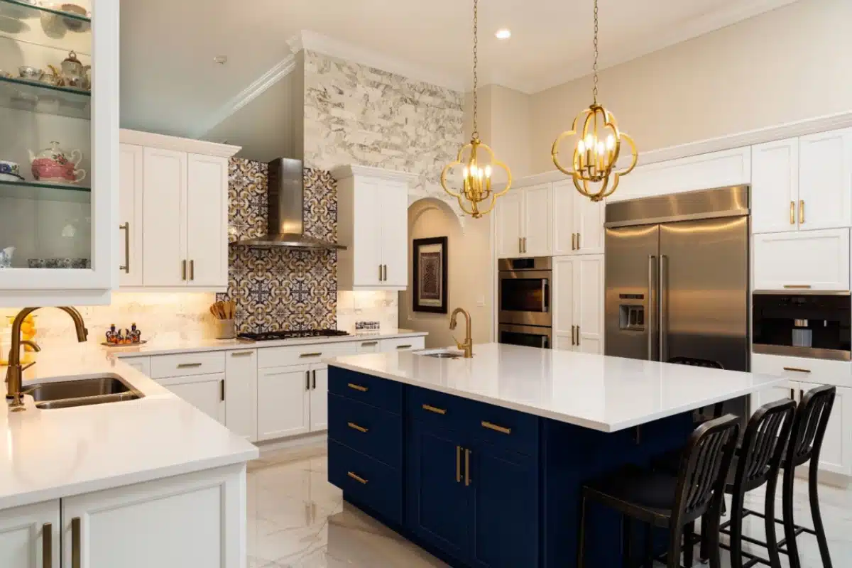 Luxury kitchen remodeling in Baltimore, MD featuring a spacious island, blue and white custom cabinetry, brass lighting fixtures, stainless steel appliances, and premium tile accents.