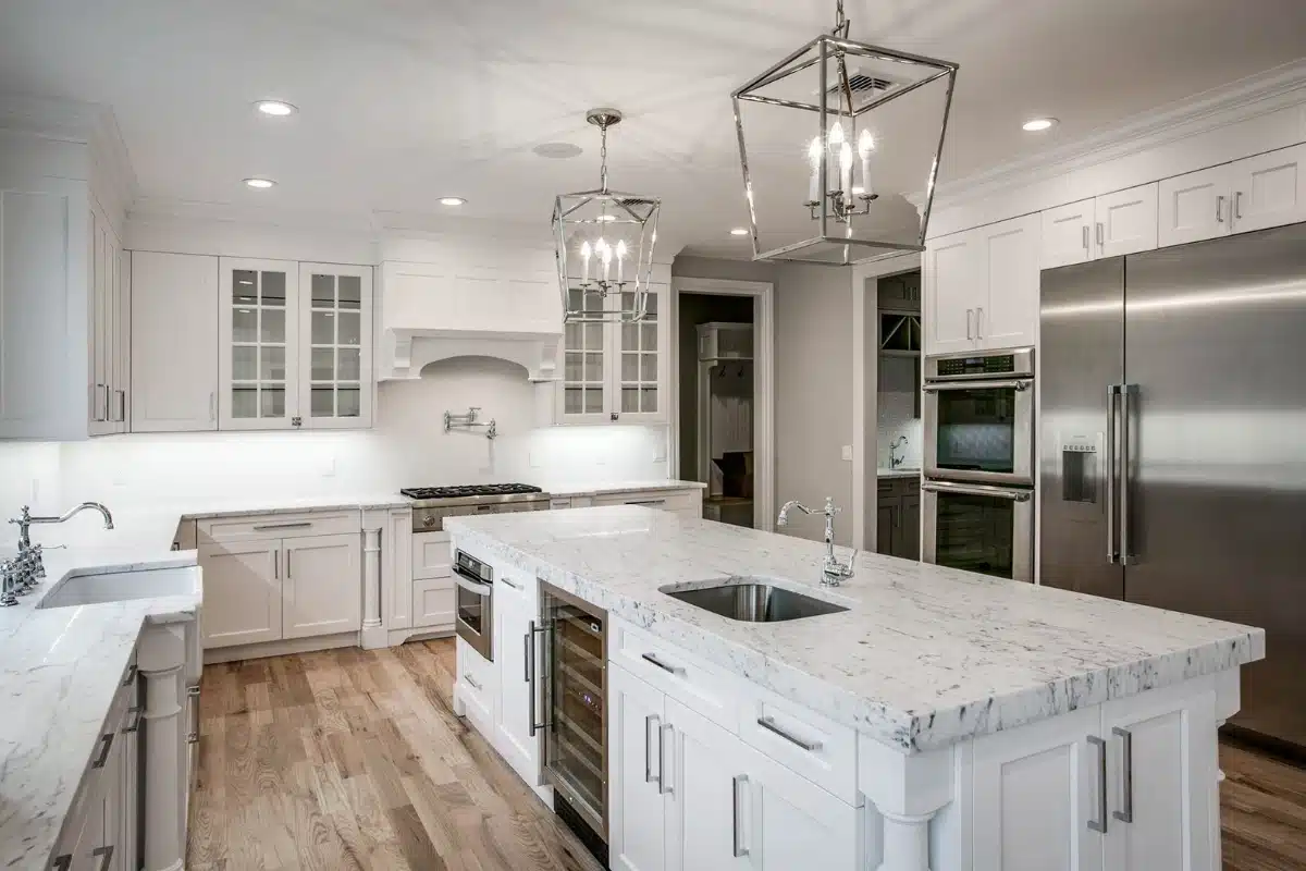 Modern kitchen showcasing new hardwood flooring replacement in Baltimore MD, featuring white cabinetry, marble countertops, and updated lighting.