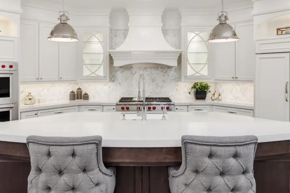 Bright luxury kitchen remodeling project in Baltimore, MD featuring white custom cabinetry, marble countertops, statement pendant lighting, and a large central island with upholstered seating.