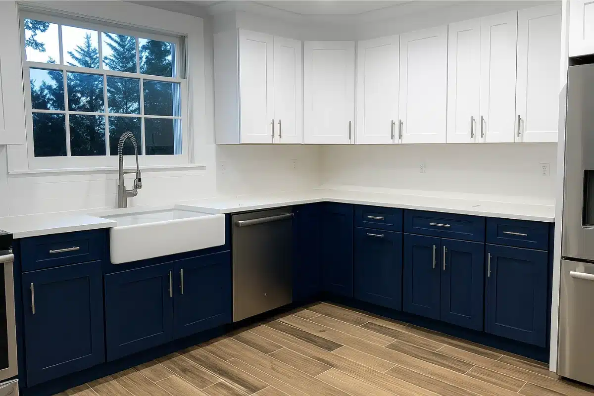 Small kitchen remodel in Baltimore MD featuring white upper cabinets, navy lower cabinets, farmhouse sink, stainless steel dishwasher, and modern wood-look flooring.