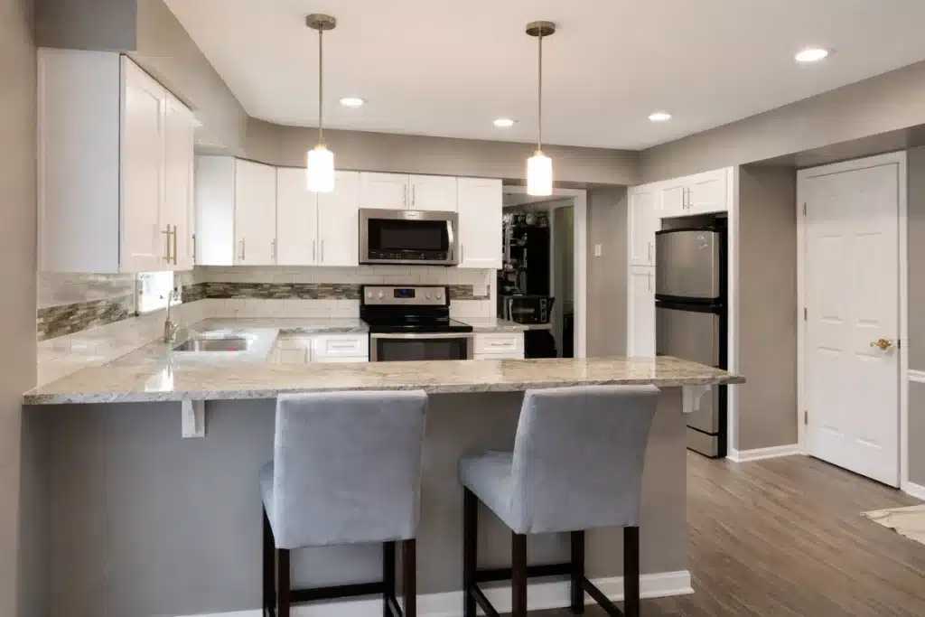 Transitional kitchen remodeling in Baltimore, MD featuring a granite breakfast bar, white cabinetry, pendant lighting, and open-concept design.