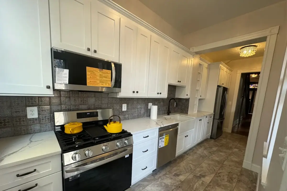 Galley-style kitchen remodeling in Cedonia, Baltimore featuring white cabinets, stainless steel appliances, tiled backsplash, and updated flooring.