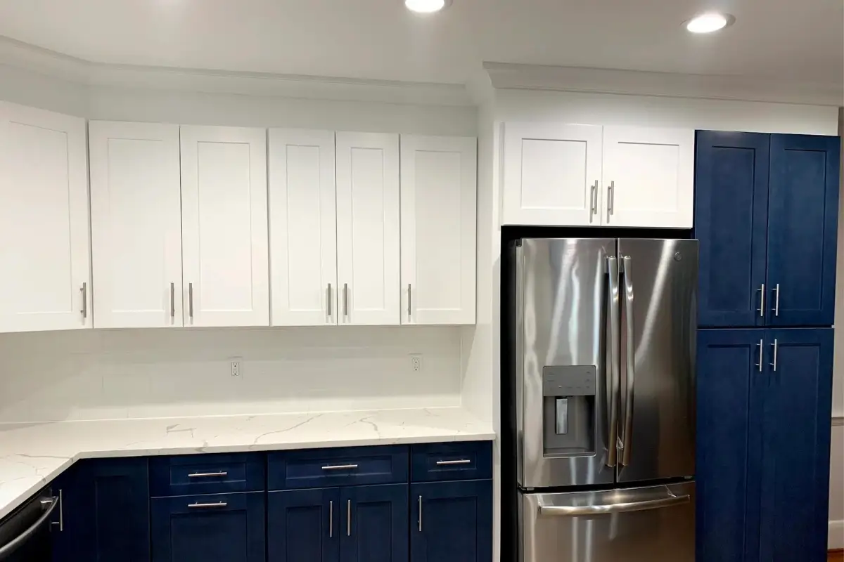 Modern kitchen remodeling project with white upper cabinets, navy blue base cabinets, and stainless steel refrigerator in Belair-Edison, Baltimore