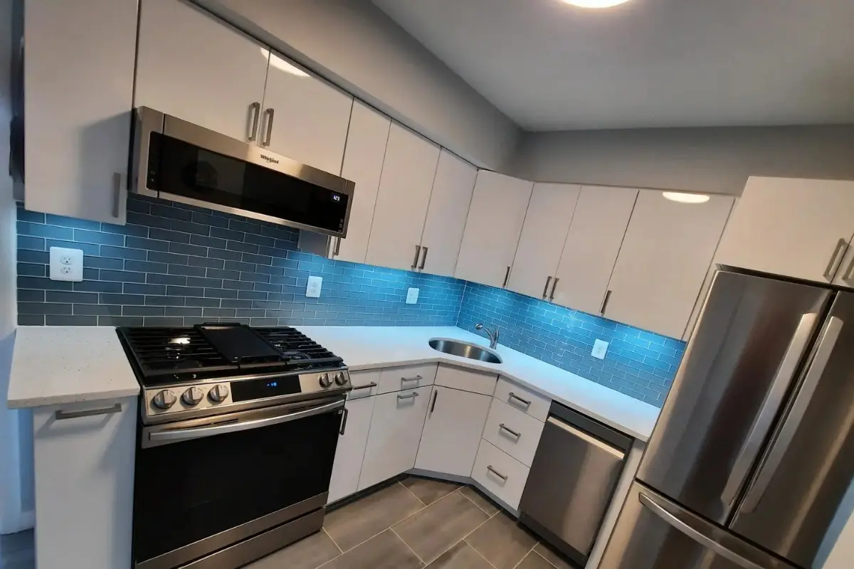 Modern kitchen remodeling in Belair-Parkside, Baltimore with white cabinetry, stainless steel appliances, and a blue subway tile backsplash.