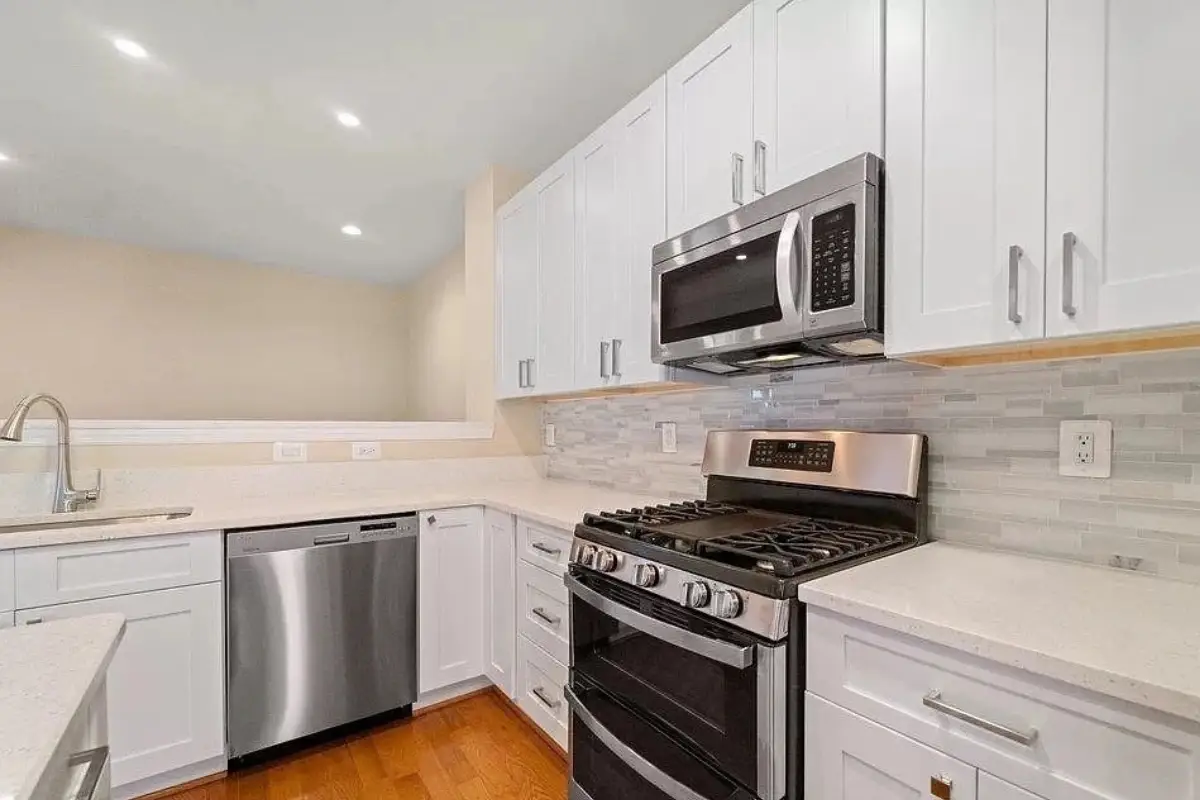Kitchen remodeling project in Mayfield, Baltimore featuring white shaker cabinets, quartz countertops, stainless steel appliances, and a light tile backsplash.