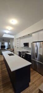 A modern kitchen remodel in Ellicott City, MD, featuring a long navy blue island with white quartz countertops, white shaker upper cabinets, stainless steel appliances, and integrated ceiling lighting.