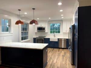 A high-end kitchen renovation in Lutherville-Timonium, MD, featuring navy blue base cabinets, white shaker uppers, white marble quartz countertops, copper dome pendant lights, and a farmhouse apron sink.
